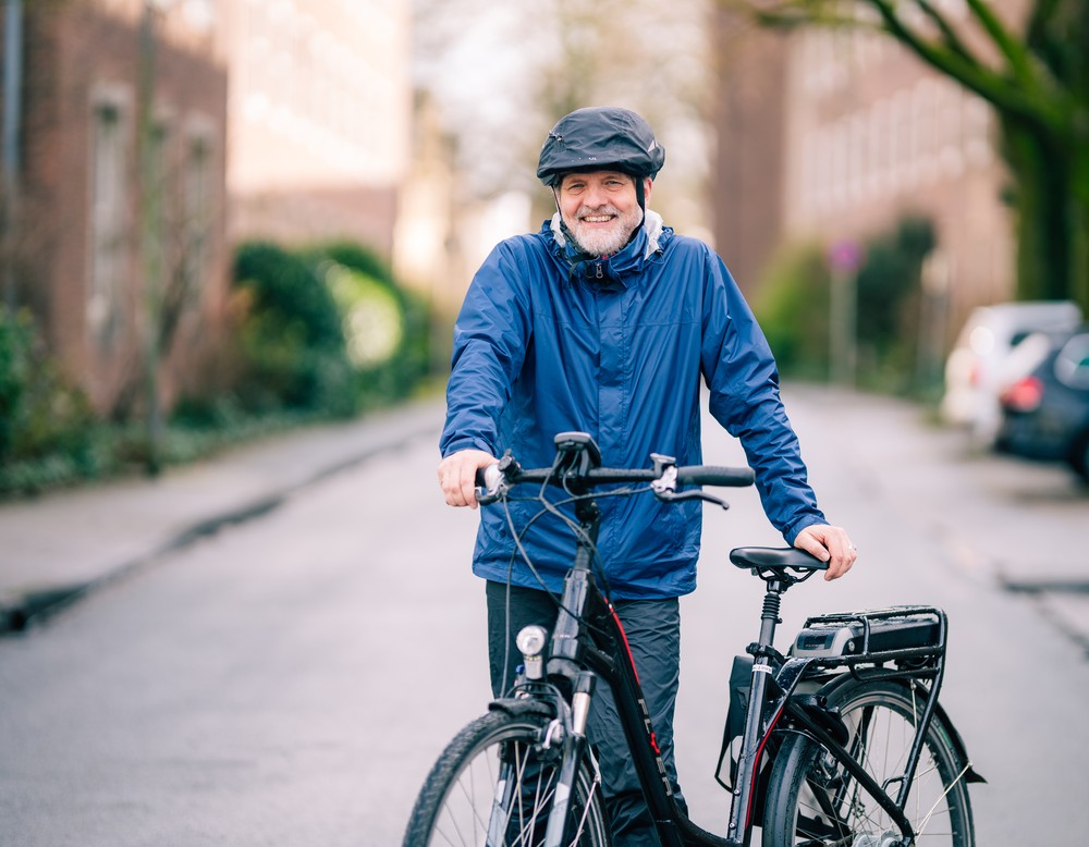 Das Bild zeigt Stefan Rütsch in einer blauen Regenjacke und mit seinem Fahrrad.