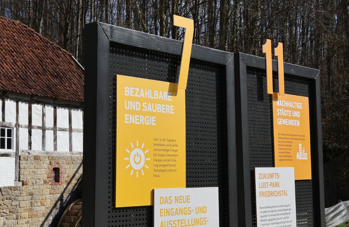 Ein Foto von zwei Infotafeln zu Klimaziel 7 und 11, im Hintergrund ein Haus von außen