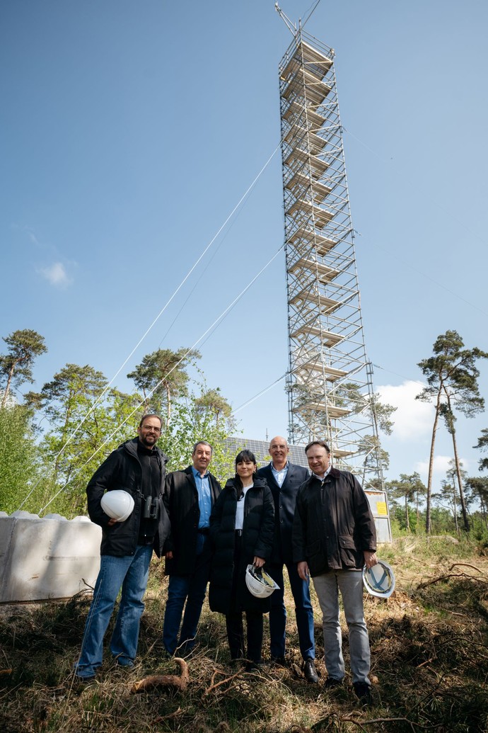 Ein Foto von 5 Personen mit Bauhelm vor einem Gerüst-Turm